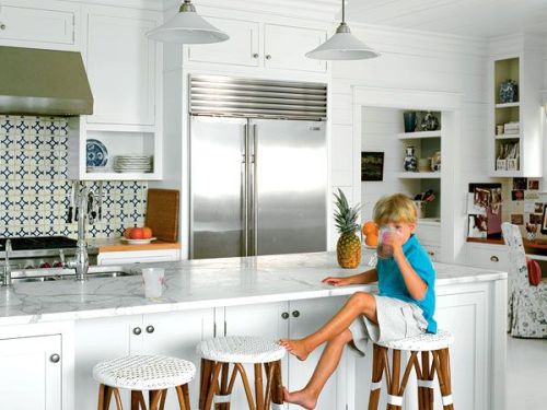 A beautiful white and green coastal kitchen with white cabinets and white carrara marble counters